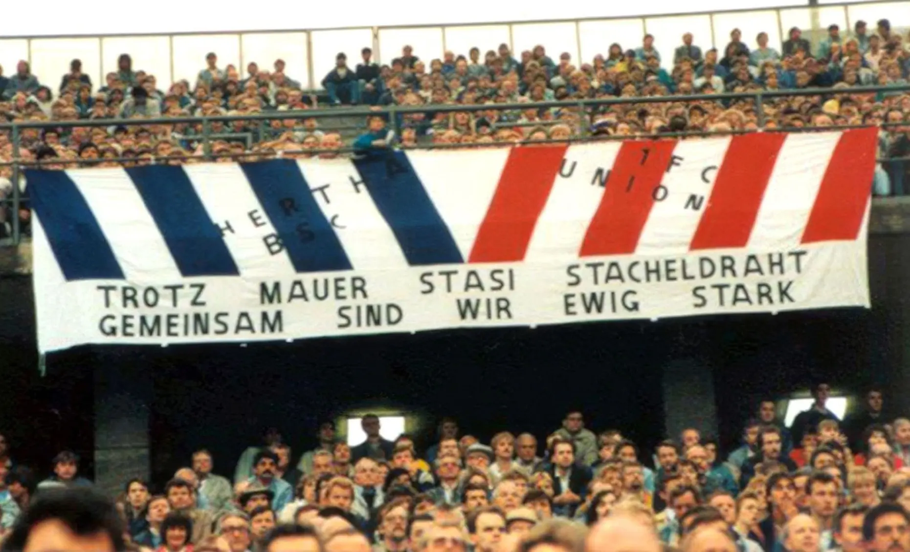 Im West-Berliner Olympiastadion wird in den 1980er Jahren ein Transparent gezeigt, dass die Fanfreundschaft zwischen Anhängern von Hertha BSC und dem 1. FC Union über die Mauer hinweg feiert. Foto: Bundesarchiv