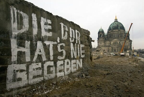 Die DDR in der Erinnerungskultur: Auf einer Mauer der Brücke Rathausstraße auf der in weißer Farbe geschrieben steht „Die DDR hat´s nie gegeben“. Im Hintergrund ist der Berliner Dom zu sehen, dazwischen die Brache, auf der einst der Palast der Republik gestanden hat. Foto: picture alliance-Arno Burgi.