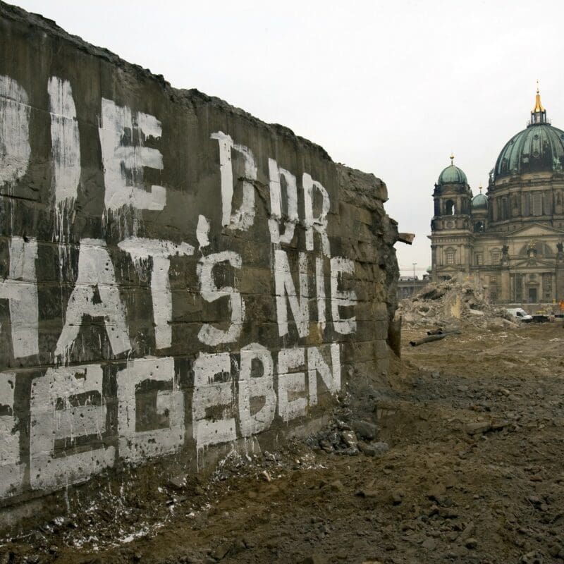 Die DDR in der Erinnerungskultur: Auf einer Mauer der Brücke Rathausstraße auf der in weißer Farbe geschrieben steht „Die DDR hat´s nie gegeben“. Im Hintergrund ist der Berliner Dom zu sehen, dazwischen die Brache, auf der einst der Palast der Republik gestanden hat. Foto: picture alliance-Arno Burgi.