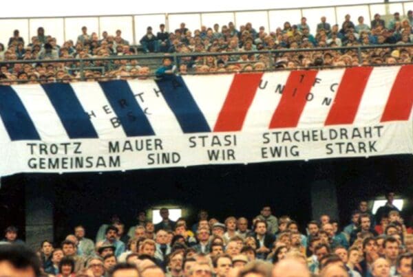Im West-Berliner Olympiastadion wird in den 1980er Jahren ein Transparent gezeigt, dass die Fanfreundschaft zwischen Anhängern von Hertha BSC und dem 1. FC Union über die Mauer hinweg feiert. Foto: Bundesarchiv