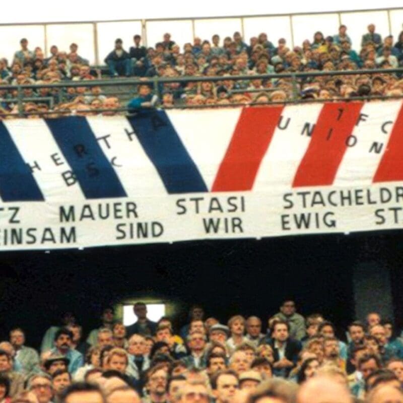 Im West-Berliner Olympiastadion wird in den 1980er Jahren ein Transparent gezeigt, dass die Fanfreundschaft zwischen Anhängern von Hertha BSC und dem 1. FC Union über die Mauer hinweg feiert. Foto: Bundesarchiv