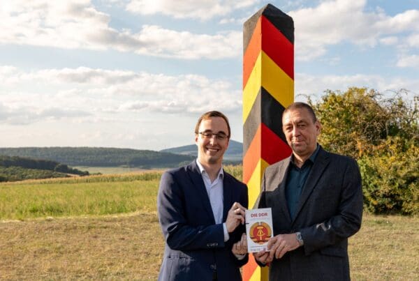 Vorstand Philipp Metzler und Referent Dr. Jens Schöne posieren vor der restaurierten Grenzsäule hinter dem Haus auf der Grenze.