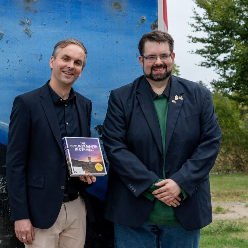 2,5 Tonnen schwer und 3,20 Meter hoch ist das Stück Berliner Mauer, das neben dem Haus auf der Grenze steht. Davor der Referent Ronny Heidenreich (links) mit der Buchausgabe „Die Berliner Mauer in der Welt“ und Jan Ludwig Antoni von der Point Alpha Stiftung. Foto: Johannes Schneider